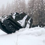 BvS10 articulated all-terrain vehicle with tracks climbing over a snow bank in a snowy forest
