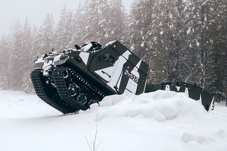 BvS10 articulated all-terrain vehicle with tracks climbing over a snow bank in a snowy forest