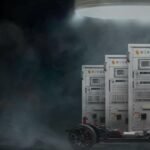 Exeliq high-voltage battery-test cabinets beside an electric-vehicle chassis