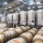 Winery production hall with stainless steel tanks and oak barrels, 1200x630 cover