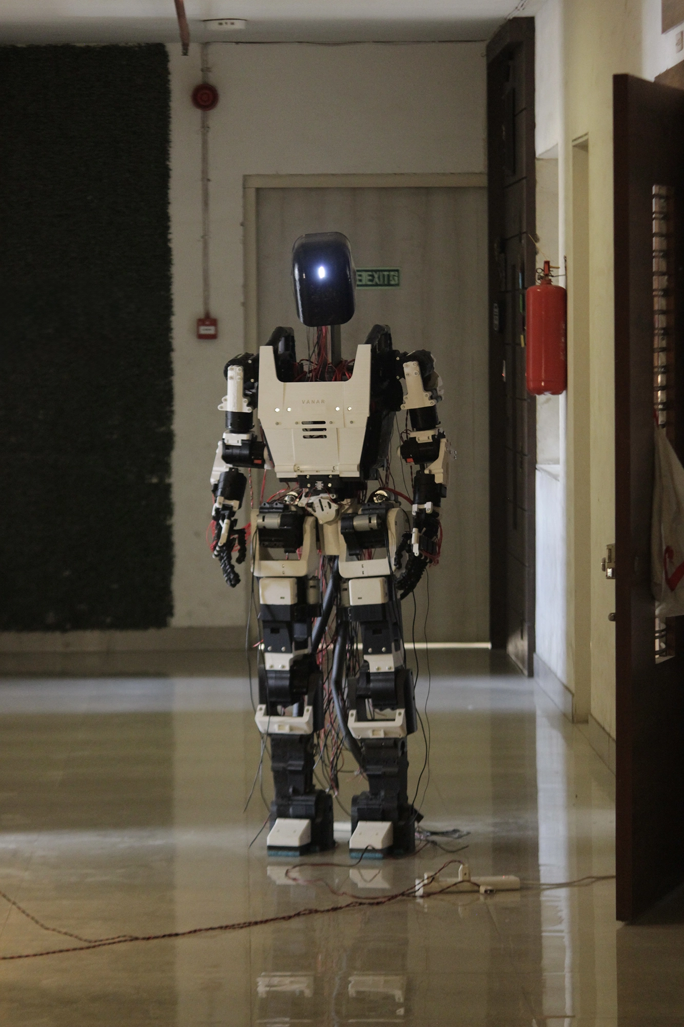 Alt text: Vanar Generation 1 humanoid robot prototype standing in a corridor with exposed wiring